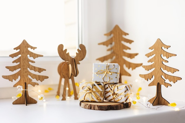 Ciervo de Navidad. Caja de regalo dorada decorativa y juguete de renos de madera en el alféizar de la ventana blanca en casa. Feliz año nuevo 2022. Figura artesanal ciervo y abeto. Bricolaje de estilo ecológico.