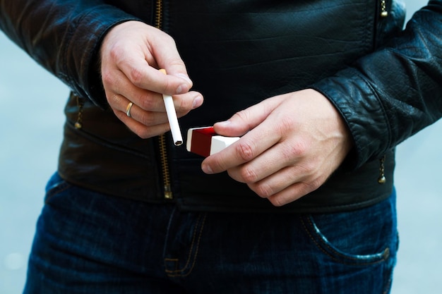 Cigarrillo ardiendo en manos masculinas al aire libre.