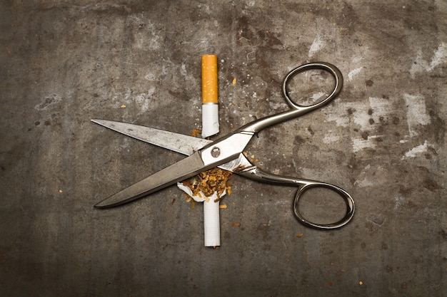 Un cigarrillo roto y unas tijeras sobre un fondo de metal oxidado