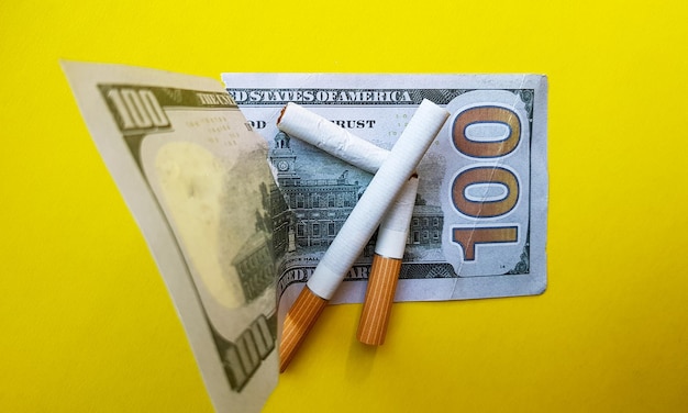 Los cigarrillos clásicos se encuentran en los billetes de cien dólares estadounidenses Los cigarrilos en un billete de cien dólares sobre un fondo amarillo