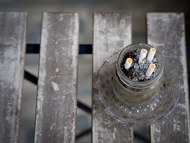 Cigarros e sucatas no cinzeiro na mesa de madeira, suja e fumaça, na área de fumar