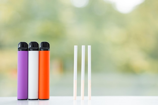 Cigarros eletrônicos descartáveis coloridos e cigarros regulares de nicotina em uma escolha de fundo verde de verão do conceito de fumo moderno