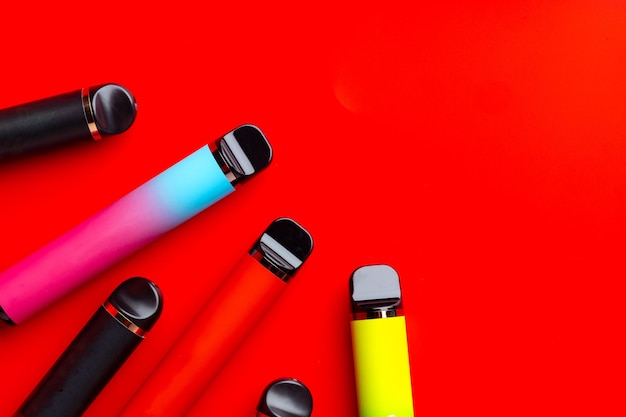 Cigarros eletrônicos descartáveis coloridos em fundo vermelho