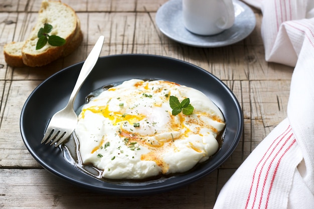 Cilbir, pochiertes Ei in Joghurt mit gewürzter Butter und Kräutern, serviert mit Brot und einer Tasse Kaffee.