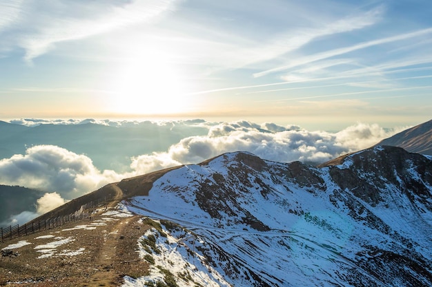 Cima de la alta montaña nevada a través de las nubes en el cielo al atardecer