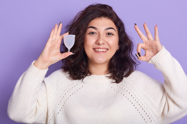 Foto cima, de, retrato, de, mulher jovem, segurando, copo menstrual, silício, isolado, sobre, parede lilás, mostrando sinal ok