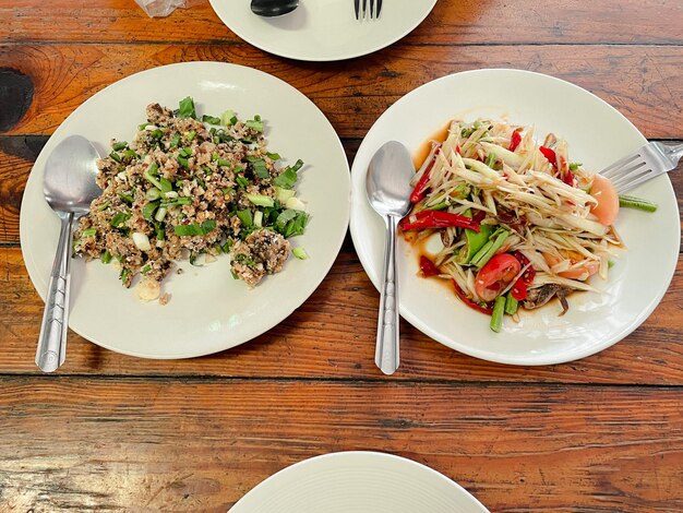 cima de ensalada de bagre picante y ensalada de papaya en un plato blanco en una mesa de madera en el concepto de comida plana