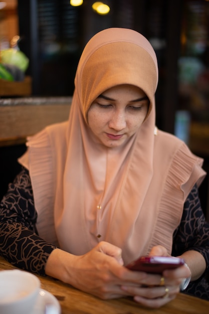 Cima, foto, de, único, muçulmano, mulher, vestido, com, marrom, hijab, jogando telefone móvel