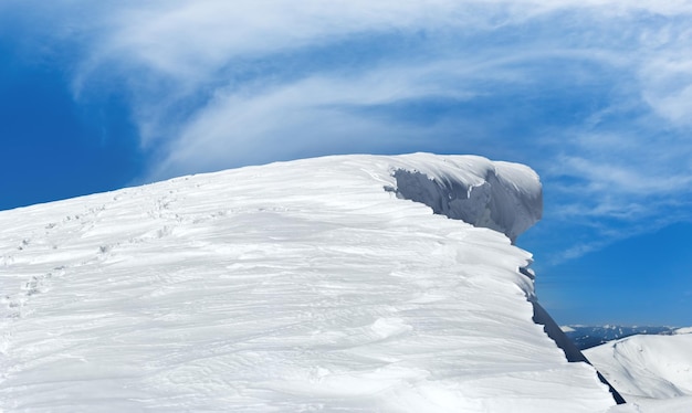 Cima de la montaña de invierno con capa de nieve colgante de hadas y huella humana en la ladera de la montaña nevada