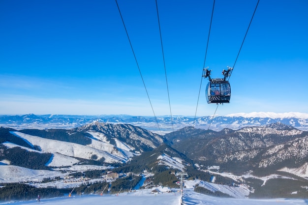 Las cimas de las montañas invernales. Tiempo soleado. Cabina del remonte contra el cielo azul. Pistas de esquí debajo