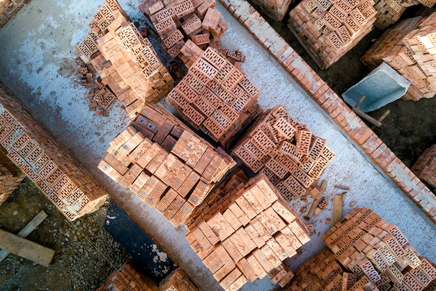 Cimientos de hormigón del sótano o primer piso de la futura casa con pilas de ladrillos rojos para la construcción de muros en un día soleado de verano, vista aérea.