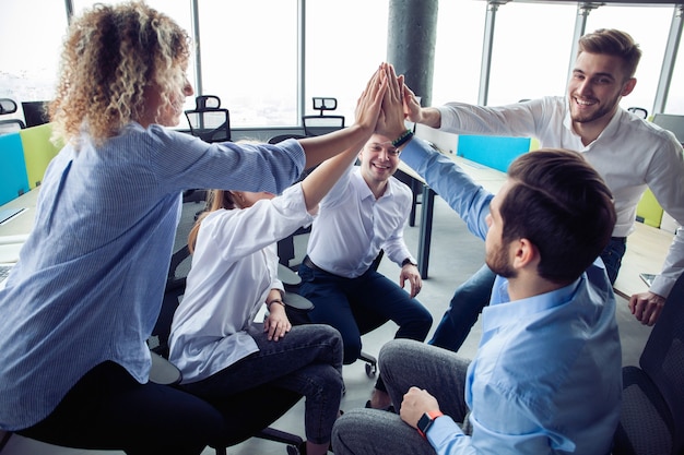 Foto ¡cinco altos! alegres jóvenes empresarios dando cinco mientras sus colegas los miran y sonríen.