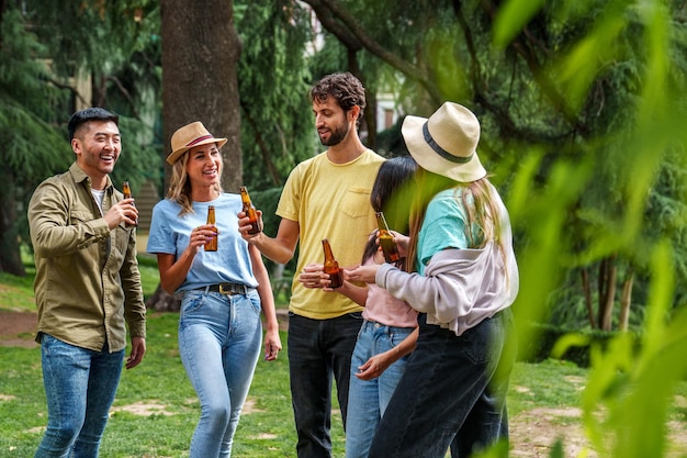 Cinco amigos diversos comparten risas con cervezas en el parque un hombre asiático con chaqueta caqui