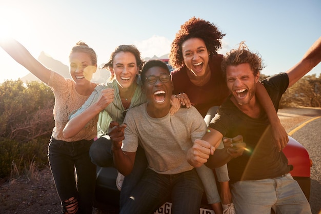 Cinco amigos do milênio em uma viagem de carro fazendo uma pausa inclinada no carro acenando para a câmera de perto