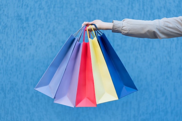 Cinco bolsas de colores para ir de compras en una mano femenina. De cerca. Compras