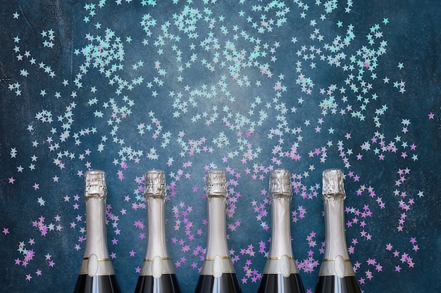 Cinco botellas de champán con estrellas de confeti holográficas en azul. Copie el espacio, vista superior