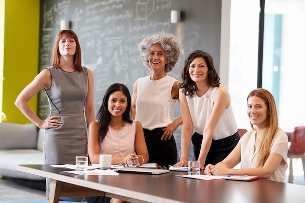 Cinco colegas do sexo feminino em uma reunião de trabalho sorrindo para a câmera