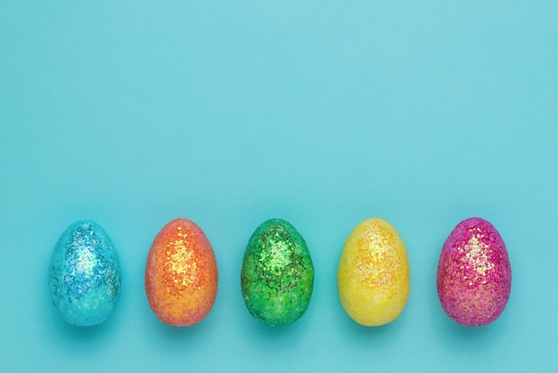 Cinco coloridos huevos de Pascua sobre un fondo azul. El concepto de vacaciones de Semana Santa. Endecha plana.