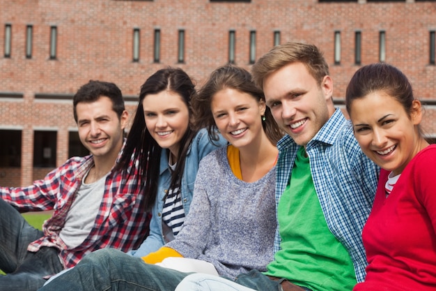 Cinco estudiantes sentados en la hierba sonriendo a la cámara