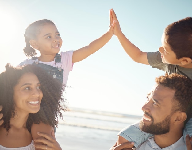 Cinco filhos e pais na praia de férias e aproveitando o dia ensolarado Pai e mãe da família em um dia fora pelo oceano com as crianças nas costas brincando e sorrindo