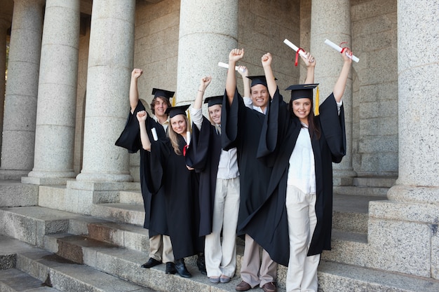 Cinco graduados felices posando los brazos levantados