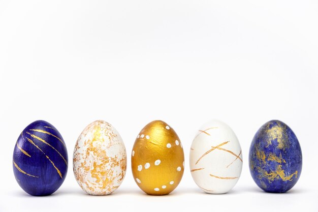 Cinco huevos de pascua de color azul, blanco y dorado sobre blanco