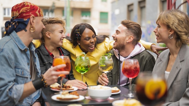 Foto cinco jovens felizes aproveitando o tempo juntos, diversos estudantes de cultura celebrando algo no pub, bebendo coquetel e comendo lanche, inclusão social, conceito de orgulho multicultural e gay