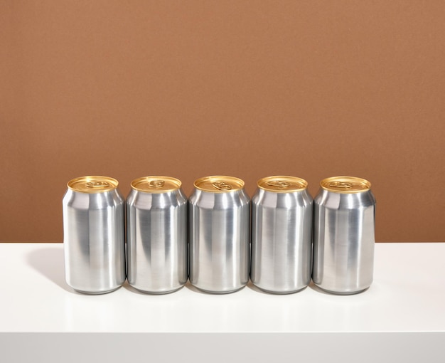 Cinco latas de aluminio de bebidas carbonatadas colocadas en fila sobre una mesa blanca Latas de aluminio realistas