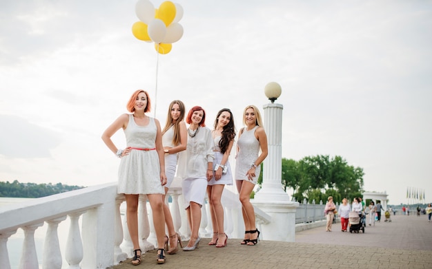 Cinco mulheres com balões à mão weared em vestidos brancos na festa da galinha contra o cais no lago.