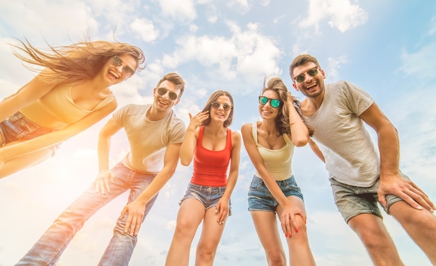 Las cinco personas felices miran a la cámara sobre el fondo de nubes azules