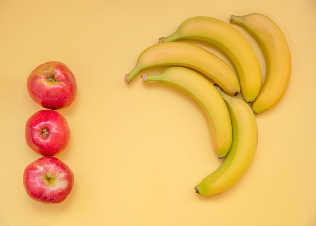 Cinco plátanos y tres manzanas yacen sobre un fondo amarillo como un marco para el texto