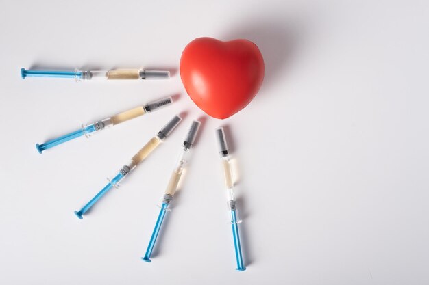 Cinco seringas com o medicamento para injeção estão ao lado de um grande coração vermelho