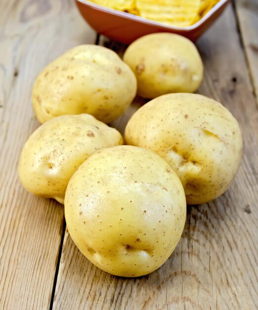 Cinco tubérculos de patata amarilla fresca, patatas fritas en un recipiente de arcilla sobre un fondo de tablas de madera