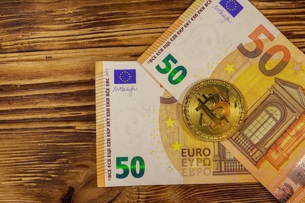 Cincuenta billetes en euros y bitcoin dorado sobre fondo de madera Vista superior