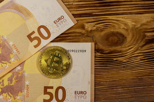 Cincuenta billetes en euros y bitcoin dorado sobre fondo de madera Vista superior