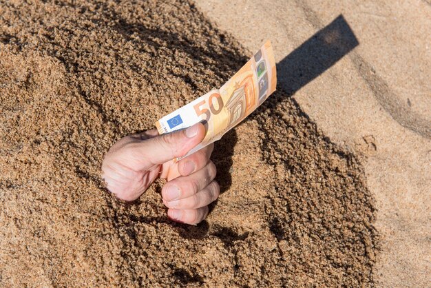 Cincuenta euros en la mano de un hombre que sobresale de la arena
