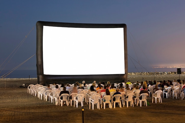 Un cine al aire libre en la playa al atardecer con sillas y gente irreconocible