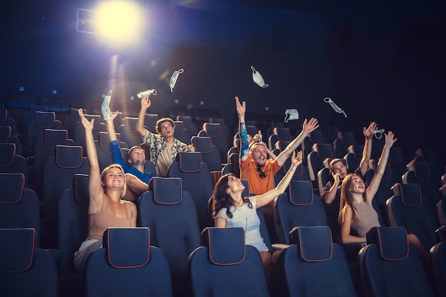 Cine en cuarentena. Reglas de seguridad para la pandemia de coronavirus, distancia social durante la visualización de películas. Hombres, mujeres con mascarilla protectora sentados en filas de auditorio. Tiempo libre, concepto de cultura juvenil.