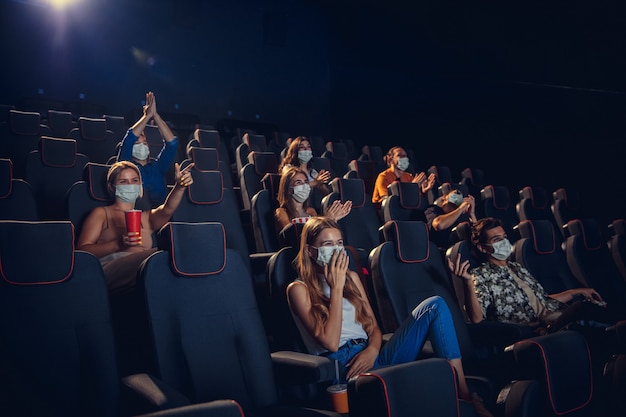 Cine en cuarentena. Reglas de seguridad para la pandemia de coronavirus, distancia social durante la visualización de películas. Hombres, mujeres con mascarilla protectora sentados en filas de auditorio. Tiempo libre, concepto de cultura juvenil.