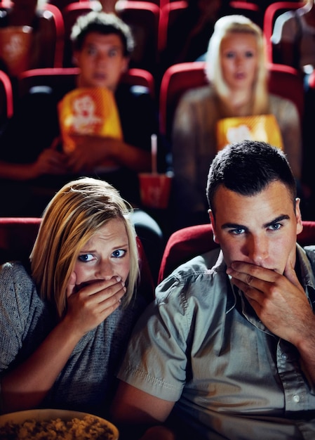 Cinema shock y pareja con palomitas de maíz viendo una película o comiendo en una cita romántica juntos noche de cine hombre y mujer en el teatro con bocadillos horror y sentados en el auditorio para relajarse en el estreno del espectáculo