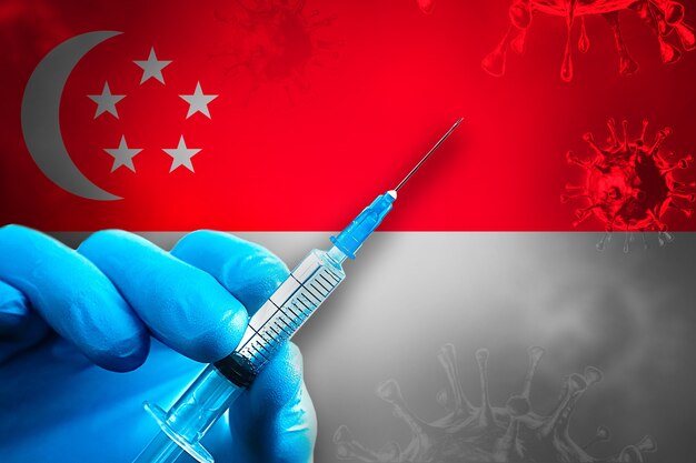 Cingapura Covid19 Campanha de vacinação Mão em uma luva de borracha azul segura uma seringa na frente da bandeira