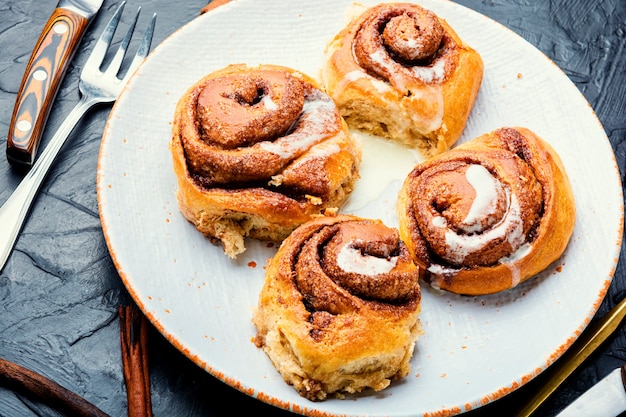 Cinnabones com canela e queijo mascarpone. Cinnabons caseiros num prato. Pãezinhos apetitosos