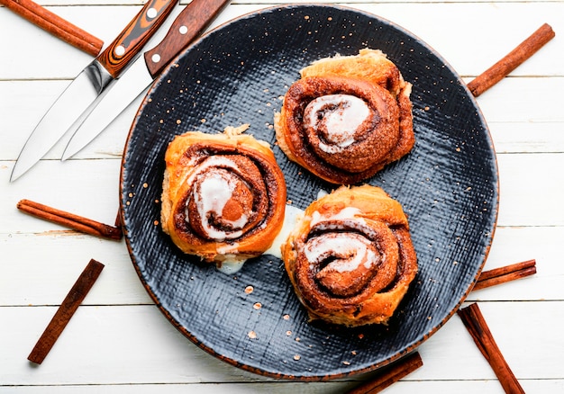 Cinnabones com canela e queijo mascarpone. Cinnabons caseiros num prato. Pãezinhos apetitosos