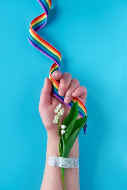 Cinta del arco iris en la mano de mujer madura con flores de lirio de los valles. Ramo adjunto con parche de asistencia médica. ¡Gracias a los médicos y enfermeras del NHS!