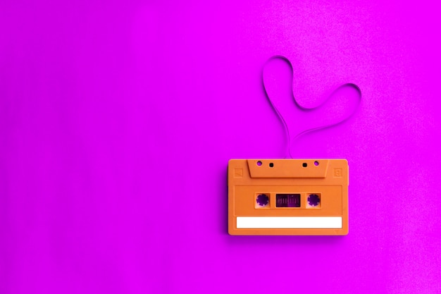 Cinta de cassette de audio antiguo con corazón de forma de película sobre fondo rosa.