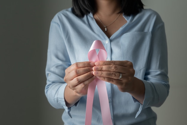 Cinta de insignia rosa en la mano de la mujer para apoyar la causa del cáncer de mama. concepto de concientización sobre el cáncer de mama