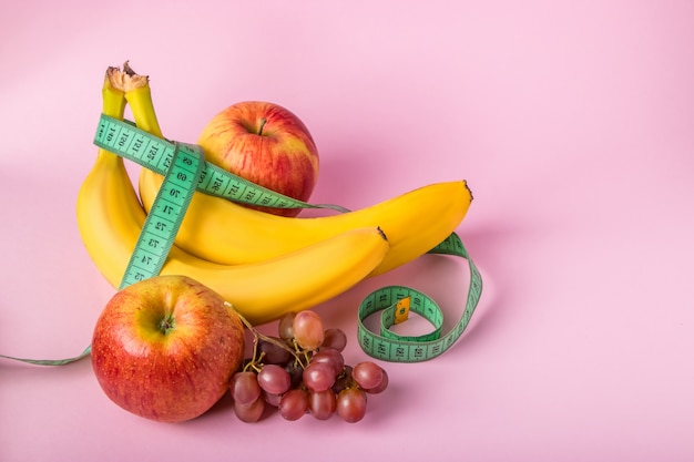 Cinta métrica y frutas jugosas en un espacio rosado. El concepto de dieta y pérdida de peso.