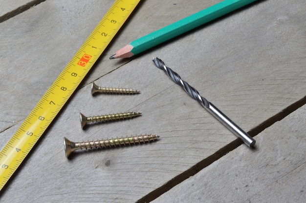 cinta métrica, lápiz y tornillos con un taladro se encuentran sobre un fondo de madera. de cerca.