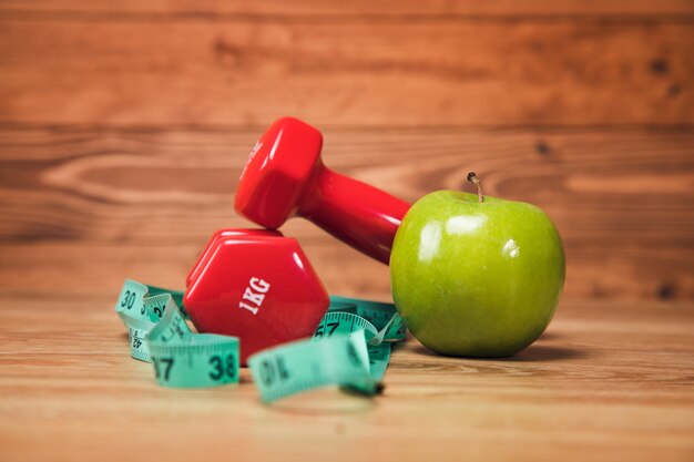 Cinta métrica, manzana y mancuernas sobre la mesa