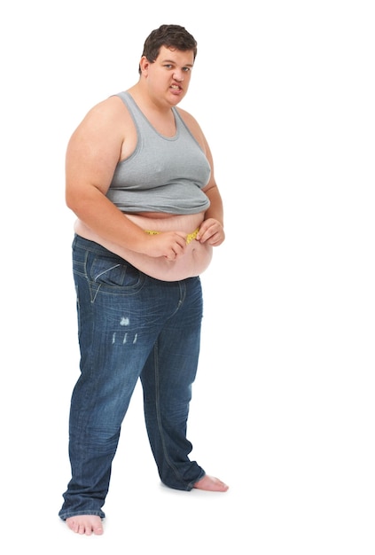 Cinta métrica de obesidad en el abdomen y el retrato de un hombre enojado que verifica la salud del cuerpo y aislado en el fondo blanco Hombre frustrado que mide el progreso de la pérdida de peso y el estómago en el fondo del estudio